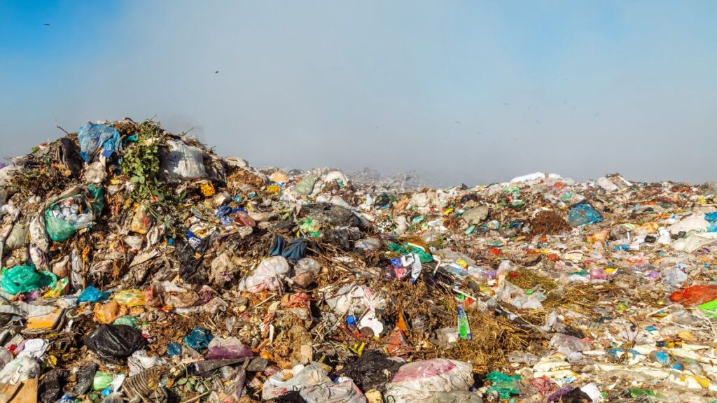 Aterro sanitário com grande volume de resíduos plásticos e orgânicos misturados, ilustrando os impactos da poluição plástica e da destinação inadequada de resíduos sólidos urbanos.